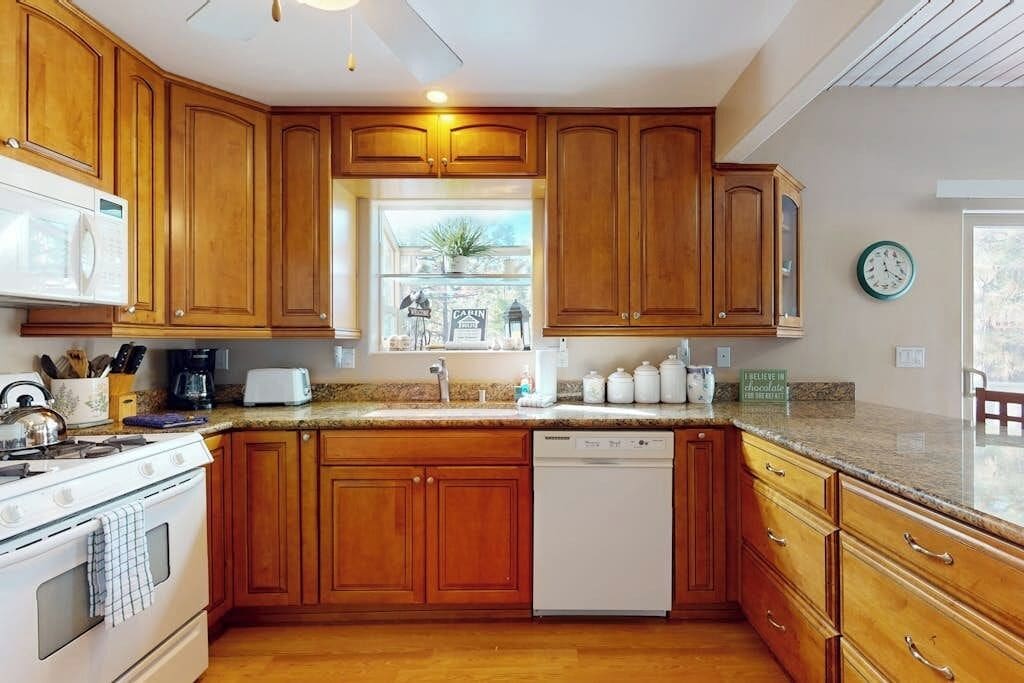 A kitchen with wooden cabinets, a microwave, a stove, a dishwasher, and a window with a view of the outside.
