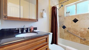 Une salle de bain avec un meuble-lavabo en bois, un évier, des toilettes et une douche dotée d’une porte en verre, ainsi qu’une fenêtre.