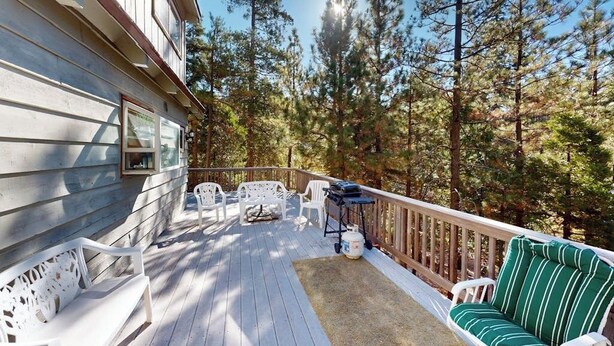 Une terrasse en bois, agréée de meubles d’extérieur, et entourée d’arbres.