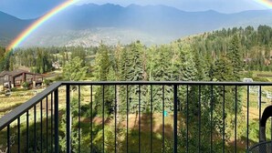 Eine Berglandschaft mit Regenbogen, einer Holzhütte und bewaldetem Gebiet.
