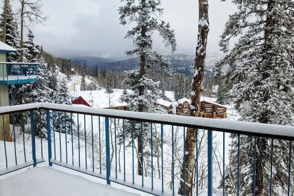 A snow-covered mountain landscape with a wooden cabin and a balcony with a blue railing.
