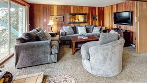 Ein Wohnzimmer mit einer Eckcouch, einem runden Sessel, einem Couchtisch, einem Fernseher und einer holzverkleideten Wand.