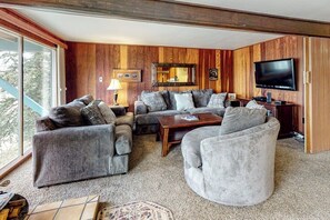 Ein Wohnzimmer mit einer Eckcouch, einem runden Sessel, einem Couchtisch, einem Fernseher und einer holzverkleideten Wand.