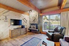 Ein gemütliches Wohnzimmer mit Kamin aus Stein, Holzbalken, einem Ledersofa und einem an der Wand befestigten Fernseher.