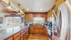 Eine Küche mit Holzausstattung, einem Edelstahlkühlschrank, Granit Arbeitsplatten und Pendelleuchten.