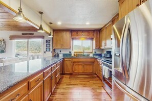 Eine Küche mit Holzausstattung, einem Edelstahlkühlschrank, Granit Arbeitsplatten und Pendelleuchten.
