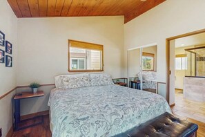 Ein Schlafzimmer mit einem Bett, einem Nachttisch mit Pflanze, einem Fenster und Blick auf einen Balkon.