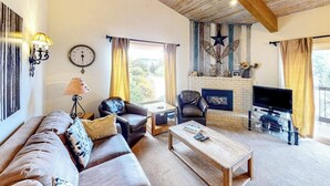 A cozy living room with a sofa, coffee table, fireplace, television, and a clock on the wall. - Spacious condo with fireplace & balcony (Snowmass Village)