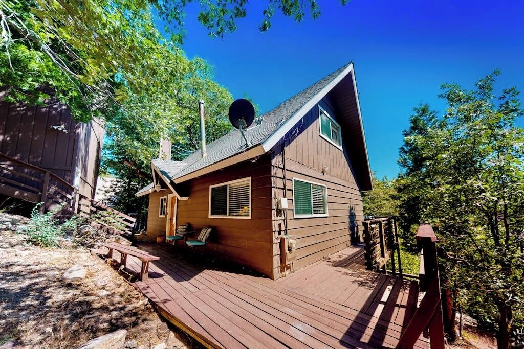 A wooden cabin with a deck, a satellite dish, and a small porch with chairs.