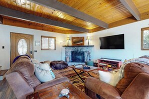 Ein gemütliches Wohnzimmer mit Kamin, Ledersofas, einem Flachbildfernseher und Holzbalken an der Decke.