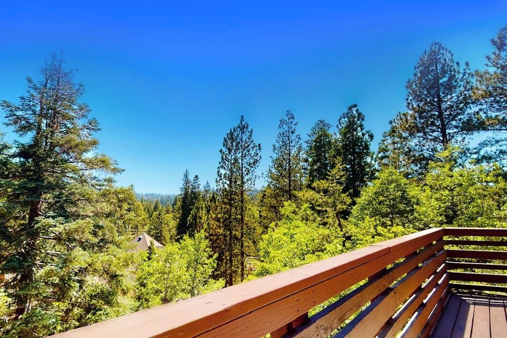 A wooden deck with a clear view of a forested area and a building in the background.
