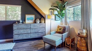 Een knusse woonkamer met een houten kast, een sofa met dessin, een klein tafeltje en een grote plant.