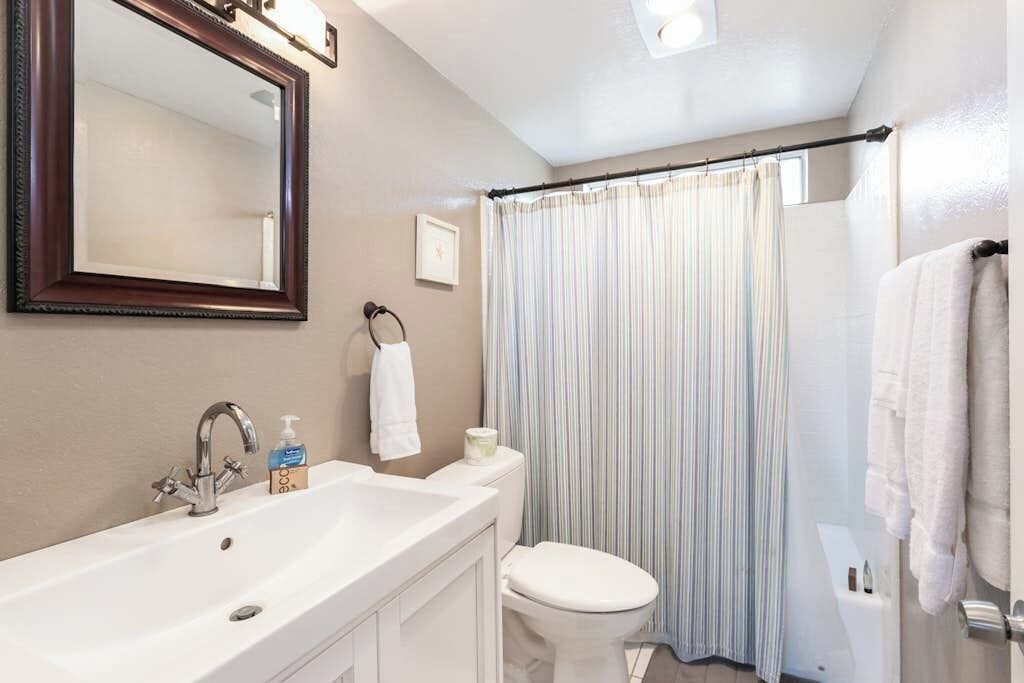 A bathroom with a white sink, a mirror, a toilet, and a shower curtain.