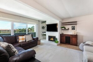 A living room with a fireplace, a television, and a large window overlooking a residential area. - Spacious Home w/ Fenced Patio, Grill & Balcony - 1 Mile to Beach & Pier Ave (Hermosa Beach)