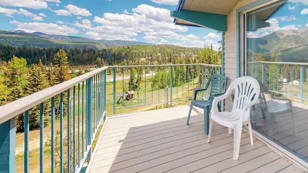 A balcony with a view of a forest and mountains, two plastic chairs, and a glass railing. - Ski-in/ski-out condo with on-site spa, balcony, fireplace & lake views (Durango)