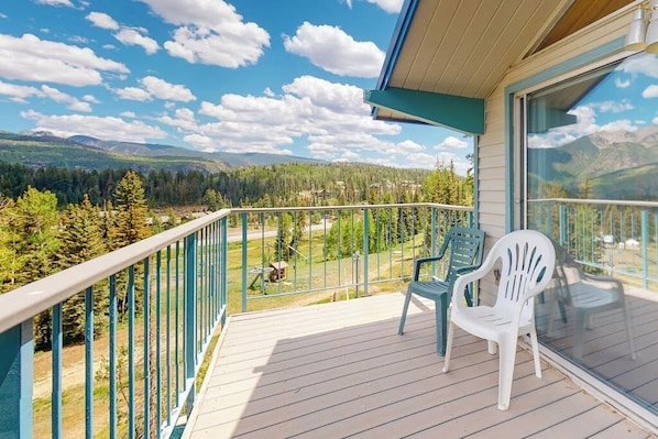 A balcony with a view of a forest and mountains, two plastic chairs, and a glass railing. - Ski-in/ski-out condo with on-site spa, balcony, fireplace & lake views (Durango)