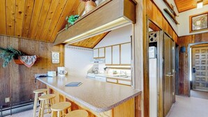 A kitchen with wooden cabinets, a central island with stools, a refrigerator, and a clock on the wall. - Ski-in/ski-out condo with on-site spa, balcony, fireplace & lake views (Durango)