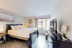 A hotel room with a bed, bedside table, lamp, TV, dresser, and a window with curtains. - Pacific Cove | Pool & Hot Tub, Fitness Center | Walk to Beach & Dining (Playa Del Rey)