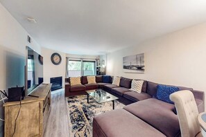 A modern living room with a sectional sofa, a coffee table, a TV, and a fireplace. - Pacific Cove | Pool & Hot Tub, Fitness Center | Walk to Beach & Dining (Playa Del Rey)