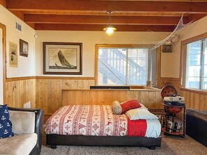Una habitación con cama, una hamaca, una ventana con vista a un edificio y un cuadro en la pared.