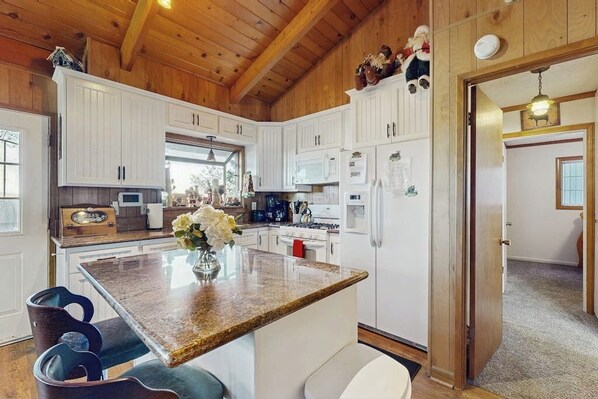 A kitchen with white cabinets, a granite countertop, and a dining area with blue chairs.