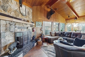 A cozy living room with a stone fireplace, leather sofas, and a mounted deer head.