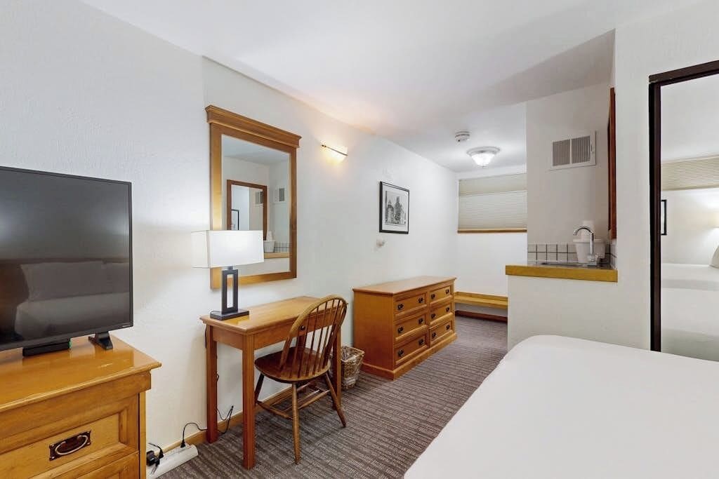 Une chambre d’hôtel comprenant un lit, un bureau avec une chaise, une télévision, une commode et un miroir.