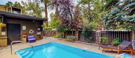 A swimming pool with a ladder, surrounded by a stone wall, trees, and a fence.