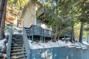 Eine Holzjagd- oder Blockhütte mit einer Treppe, die zu einer Terrasse führt, umgeben von Bäumen und Schnee.