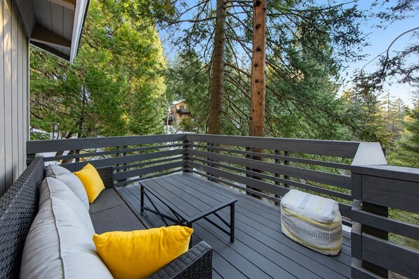 Una terraza con mobiliario exterior, incluyendo un sofá y un pouf redondo, rodeada de árboles.
