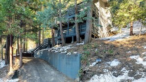 A multi-level wooden structure with a staircase leading to an upper level, surrounded by trees and a snow-covered ground. - Colorful home with washer/dryer, AC & wood-burning fireplace in a lovely setting (Lake Arrowhead)