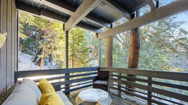 A covered outdoor seating area with a bench and cushions, overlooking a forested area. - Colorful home with washer/dryer, AC & wood-burning fireplace in a lovely setting (Lake Arrowhead)