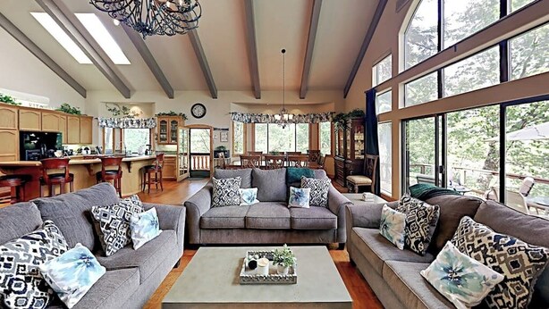 A spacious living room with a grey sofa set, a coffee table, and a chandelier. - Beautiful home W/ Lake Access, Decks, Fire pit, Papoose Lake views, & EV Charger (Lake Arrowhead)