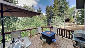 A wooden deck with a table and chairs, a fire pit, and a grill. - Beautiful home W/ Lake Access, Decks, Fire pit, Papoose Lake views, & EV Charger (Lake Arrowhead)