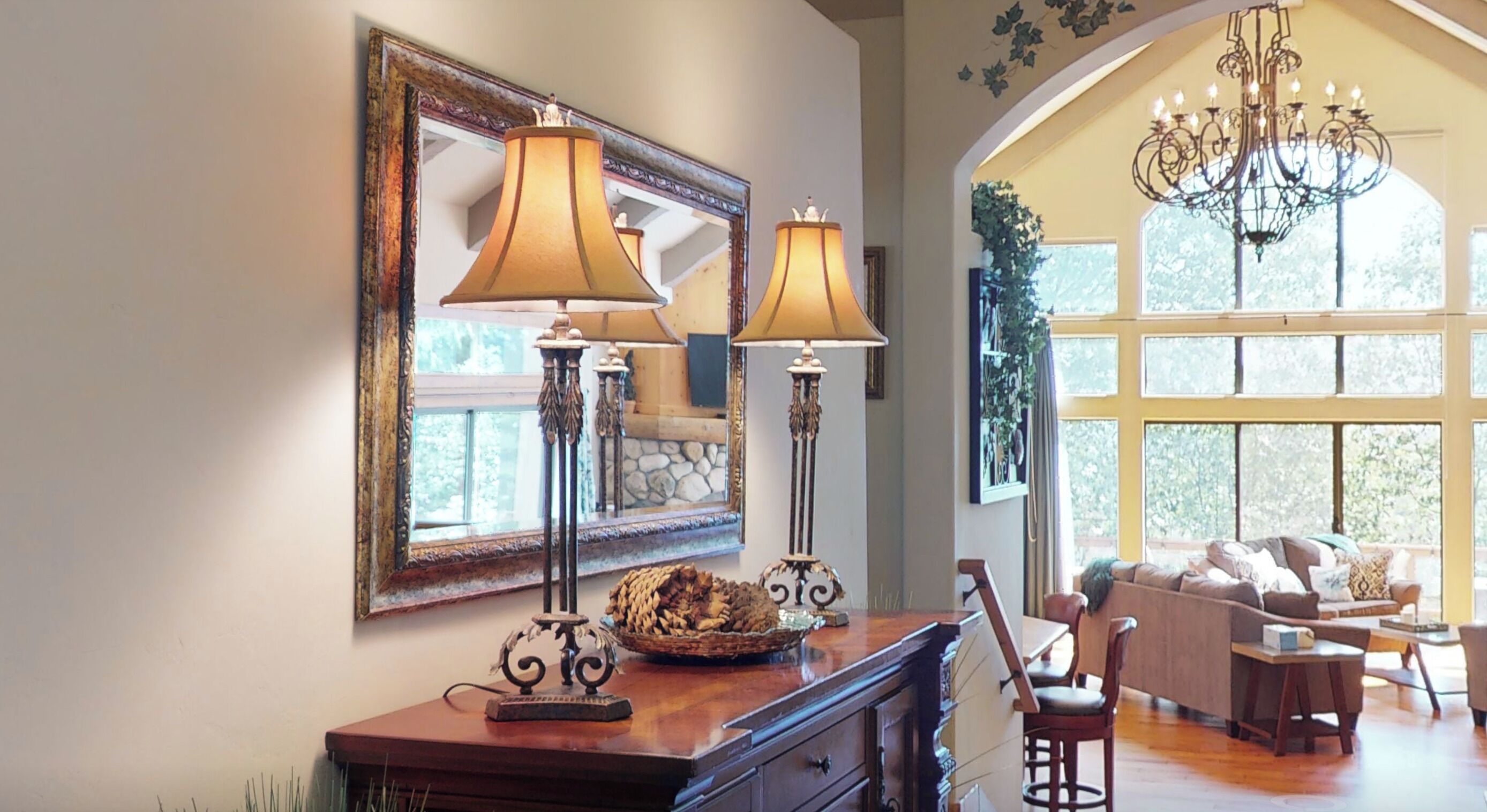 A well-lit room with a large mirror, two floor lamps, a chandelier, and a cozy seating area with a sofa and chairs.