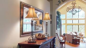 A well-lit room with a large mirror, two floor lamps, a chandelier, and a cozy seating area with a sofa and chairs.