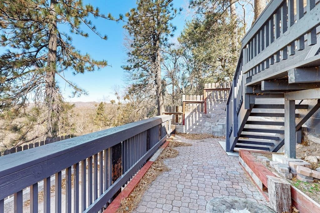 A wooden deck with a metal railing, a stone pathway, and a staircase leading to a building.