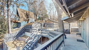 A wooden deck with a staircase leading to a covered area, surrounded by trees and a building with a sloped roof.