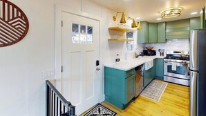 A modern kitchen with teal cabinets, stainless steel appliances, and a wooden floor.