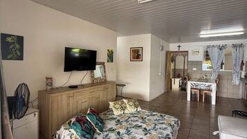 Une chambre à coucher comprenant un lit, un téléviseur, une commode en bois et un coin repas avec une table et des chaises.