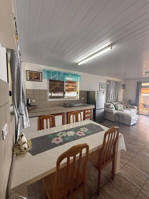 A dining area with a table, chairs, and a kitchen in the background. - Fare Holidays Raiatea (Avera, Raiatea)