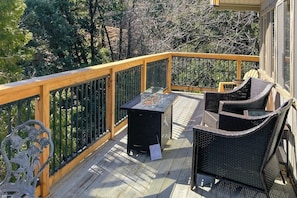 A wooden deck with a railing, outdoor furniture, and a grill.