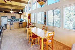 A spacious kitchen with wooden cabinets, a dining table with chairs, and large windows with blinds.