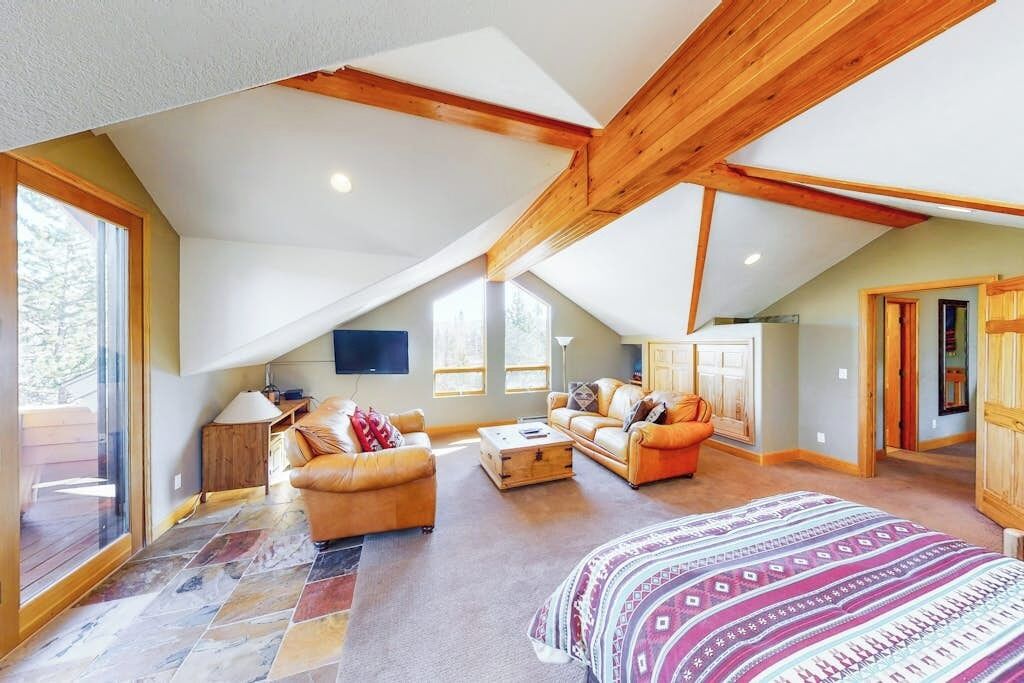 A spacious attic room with a sloped ceiling, a large bed, two sofas, a coffee table, and a television.