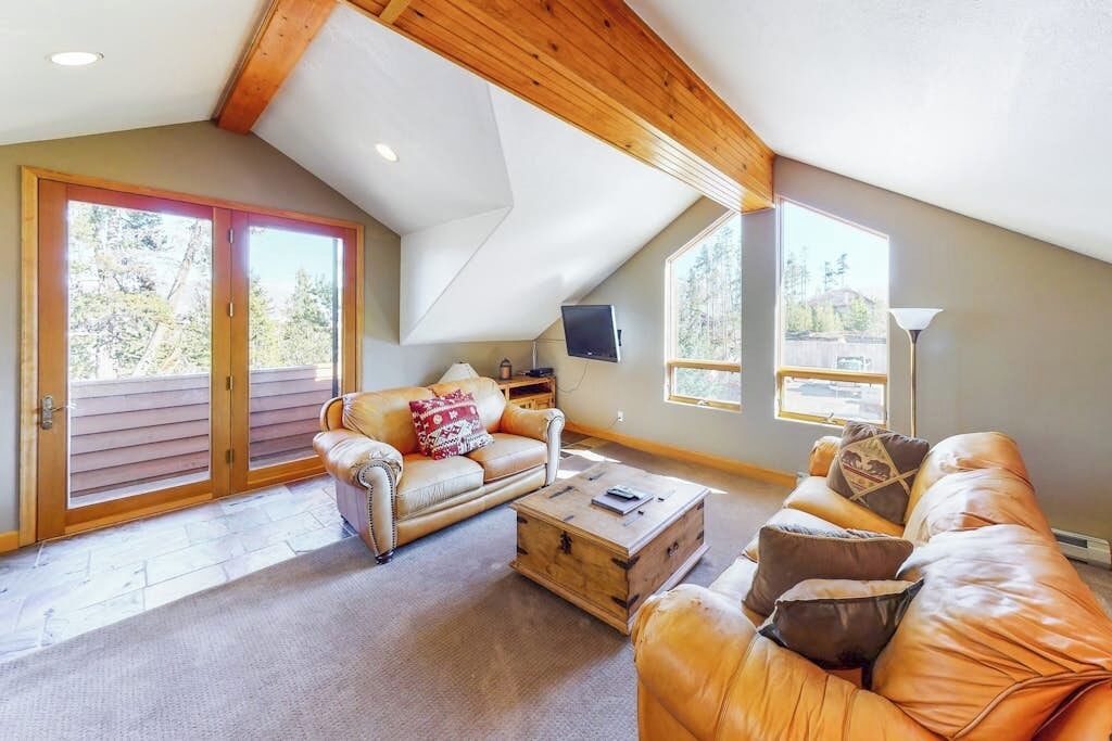A spacious living room with a high ceiling, a wooden ceiling, a large sliding glass door, a sofa, a coffee table, and a television.