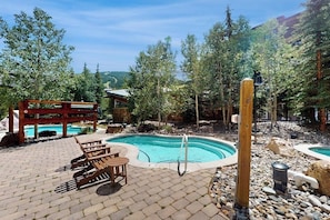 A pool area with a wooden deck, lounge chairs, and a small building with a sloped roof. - Walk to slopes - Village condo with balcony, views, hot tubs, & gym (Copper Mountain)