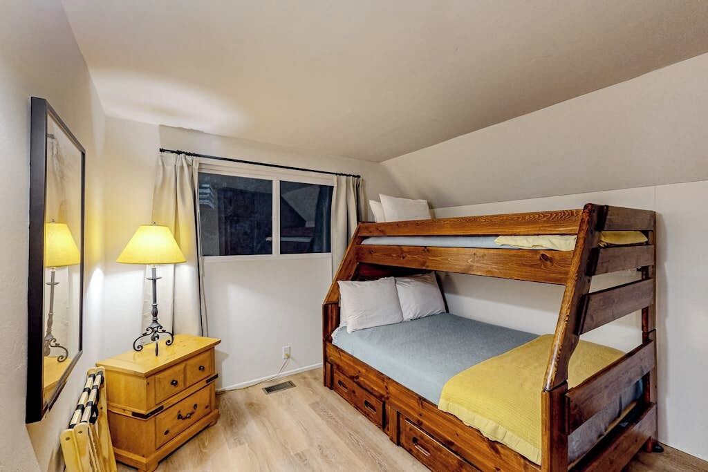 Habitació amb lliteres, un taulell de fusta, una làmpada i una finestra amb cortines.