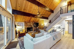 A spacious living area with a fireplace, a sofa, and a staircase leading to an upper level. - Enchanting lake retreat with fireplace, games, & great deck views - dog-friendly (Crestline)