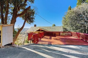 Eine Holzterrasse mit roter Geländer, ein kleines Gartenhaus und ein Haus mit geneigtem Dach.