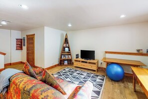 Ein Wohnzimmer mit einer Couch, einem Fernseher, einem Bücherregal, einem Schreibtisch und einem blauen Fitnessball.